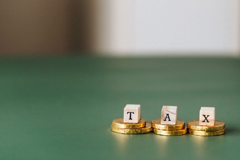 Stacked gold coins with wooden blocks spelling TAX on a green backdrop.