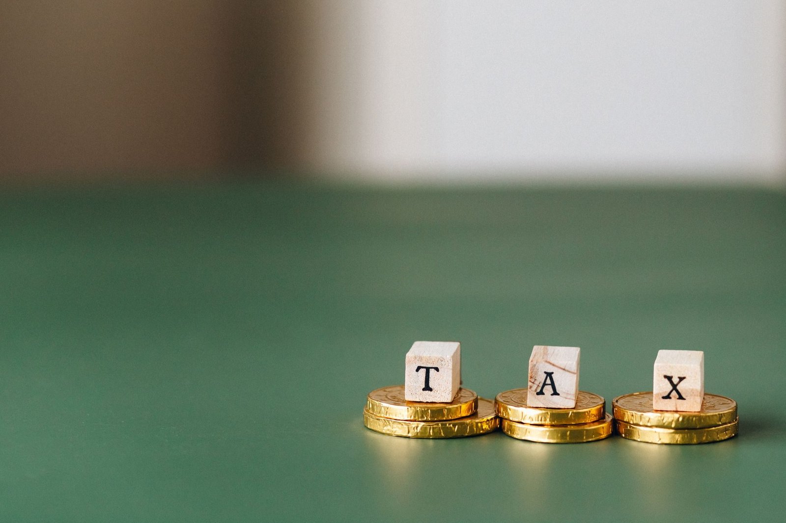Compensacao tributaria: como usar creditos para quitar debitos com o fisco 1 Stacked gold coins with wooden blocks spelling TAX on a green backdrop.