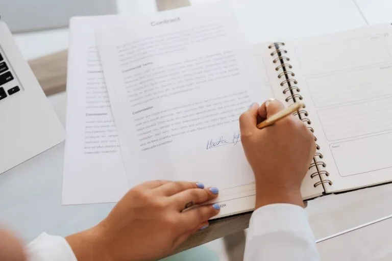 Contratos de adesão digitais: termos de uso que prendem o consumidor sem que ele perceba 7 Close-up of hands signing a contract on a desk with office supplies, symbolizing