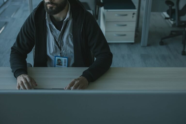 A man in a black jacket works at a desk in a modern office setting.