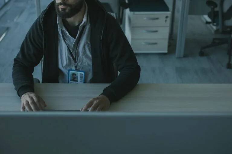 Perfil falso e roubo de identidade nas redes: como agir e responsabilizar 7 A man in a black jacket works at a desk in a modern office setting.