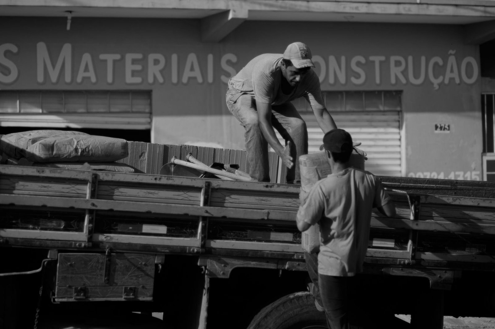 Black and white of anonymous male worker giving bag to coworker standing on trun