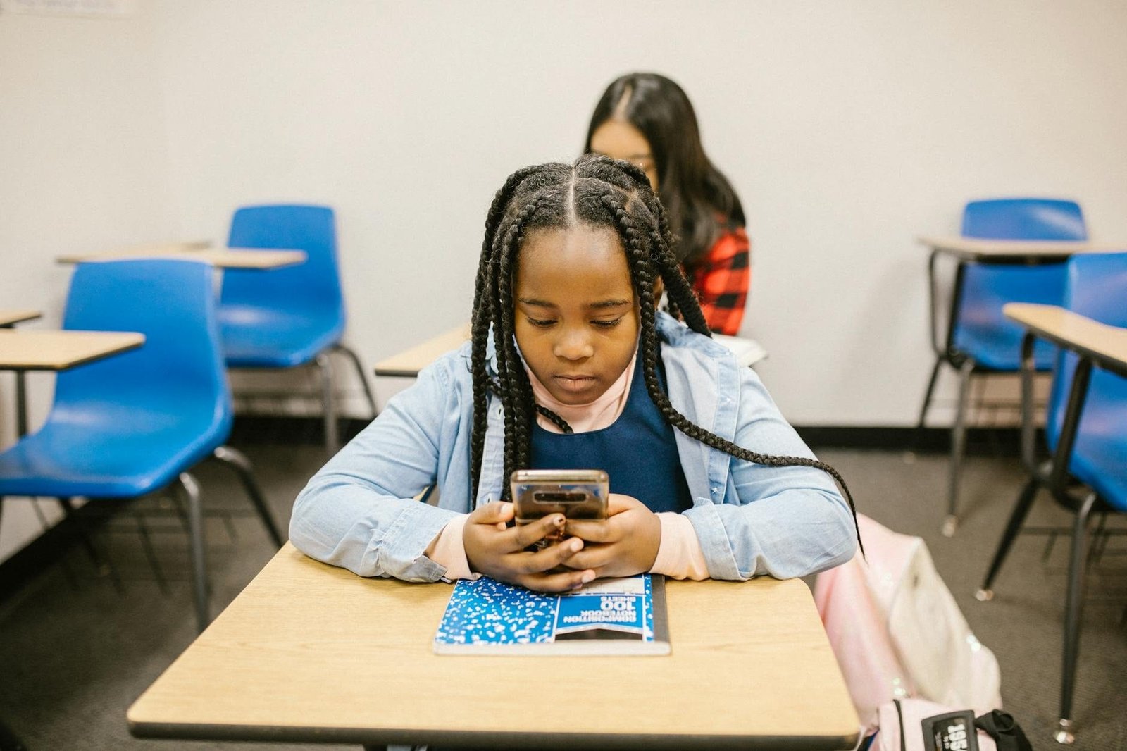 A young girl uses her smartphone while seated in a classroom environment, focused and engaged.