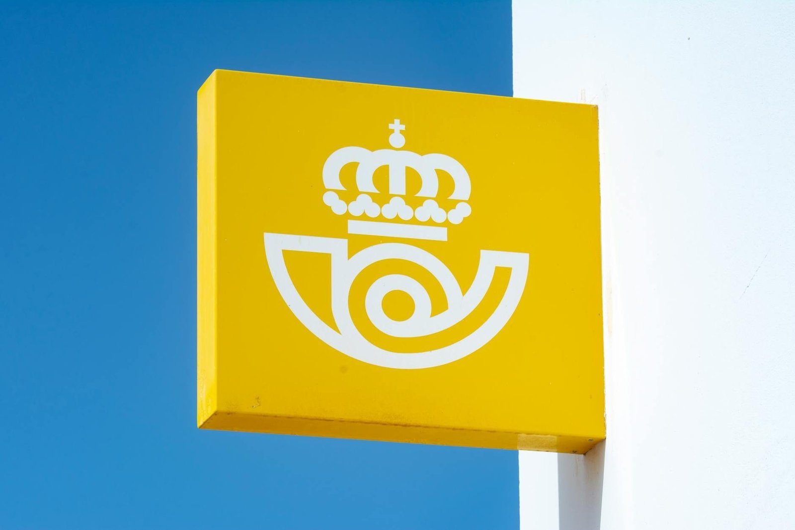 Sign for Spanish postal service against blue sky, capturing iconic symbol.