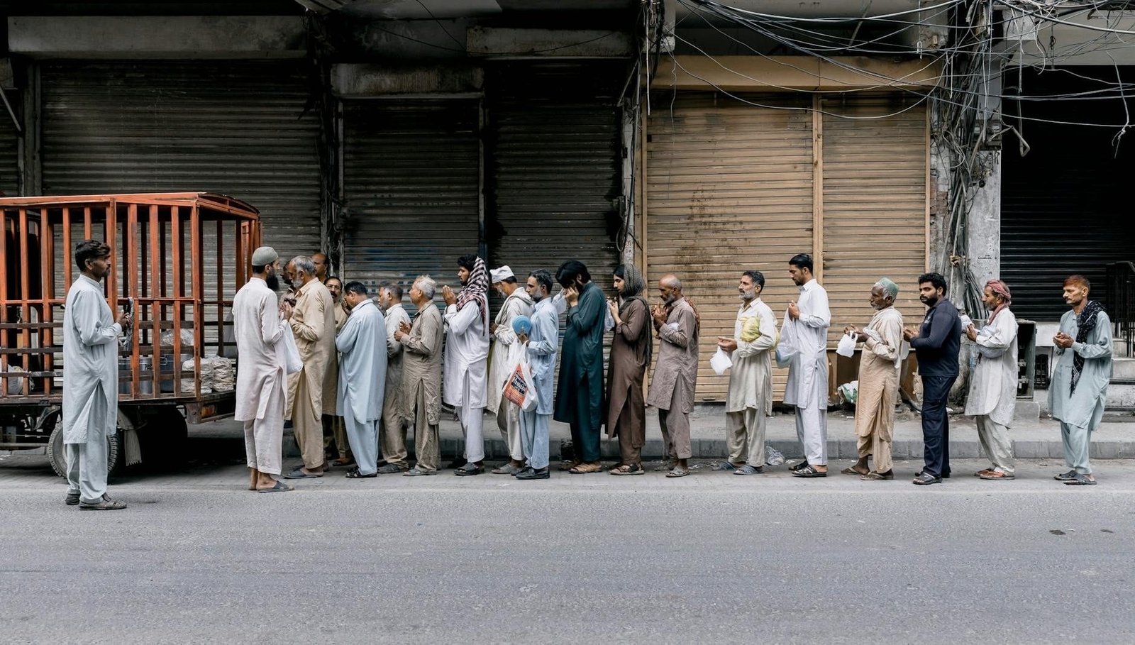 A group of adults standing in line for charity aid on a city street in Faisalabad, Pakistan.