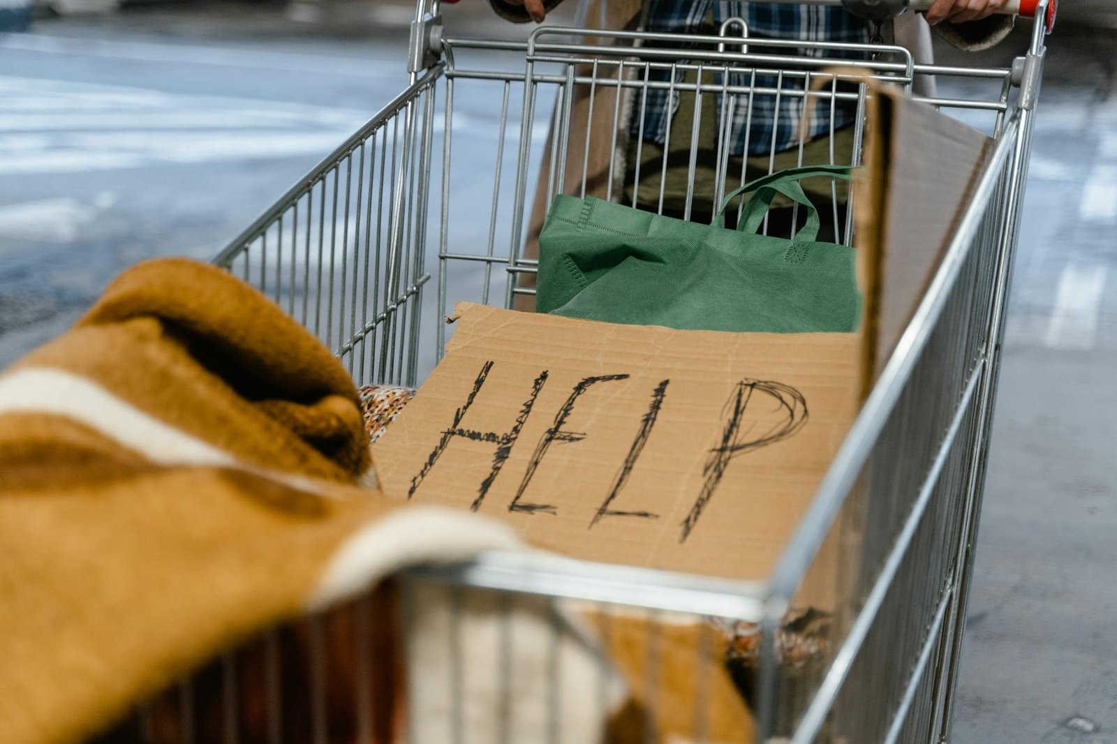 A shopping cart with a cardboard 'Help' sign and belongings, symbolizing urban homelessness.