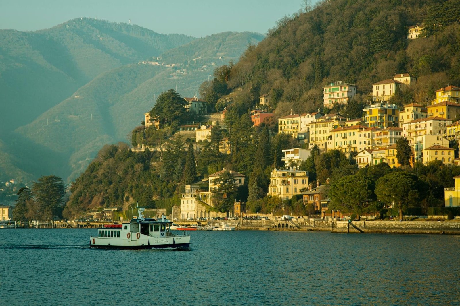 Picturesque view of Lago di Como with colorful hillside houses and a ferry in sp