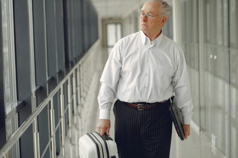 Serious senior male in formal clothes walking along airport corridor with baggag