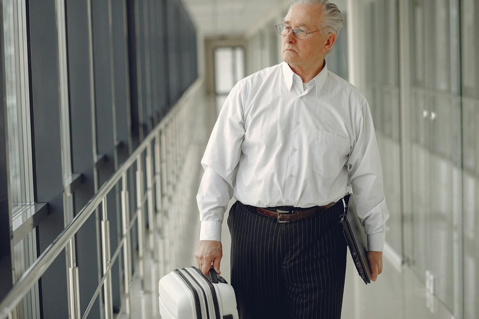 Serious senior male in formal clothes walking along airport corridor with baggag
