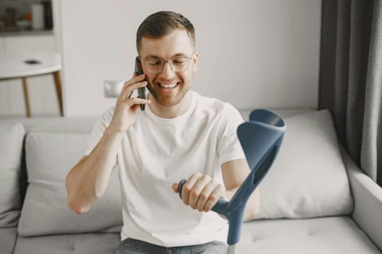 Man using crutch smiling and talking on phone indoors.
