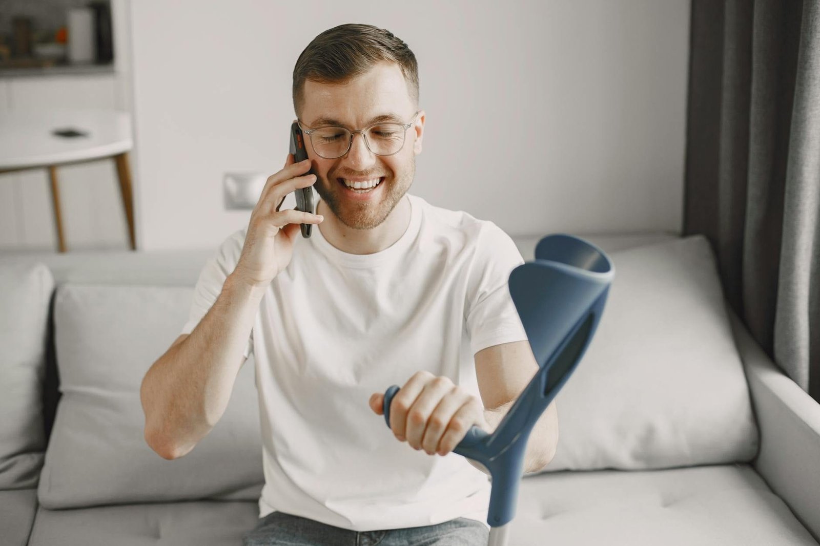 Man using crutch smiling and talking on phone indoors.