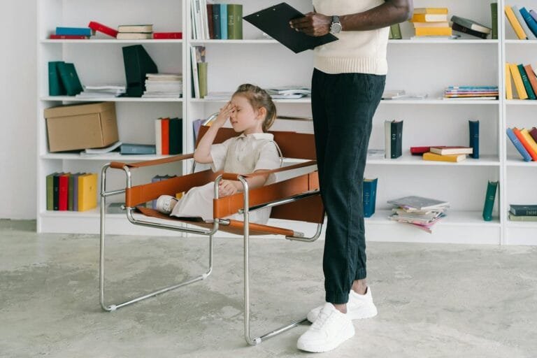 A child in a therapy session with a therapist holding a clipboard.