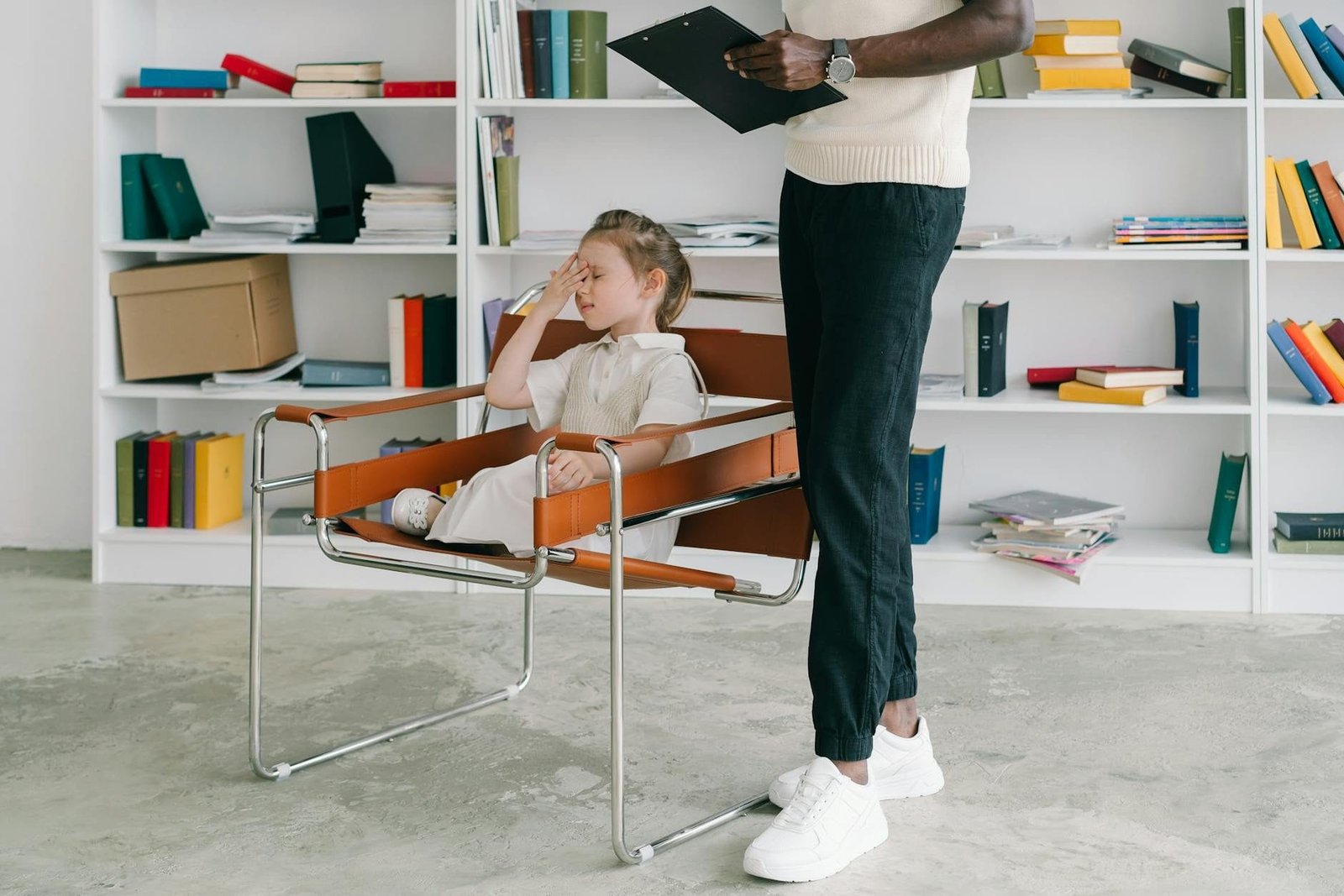 A child in a therapy session with a therapist holding a clipboard.