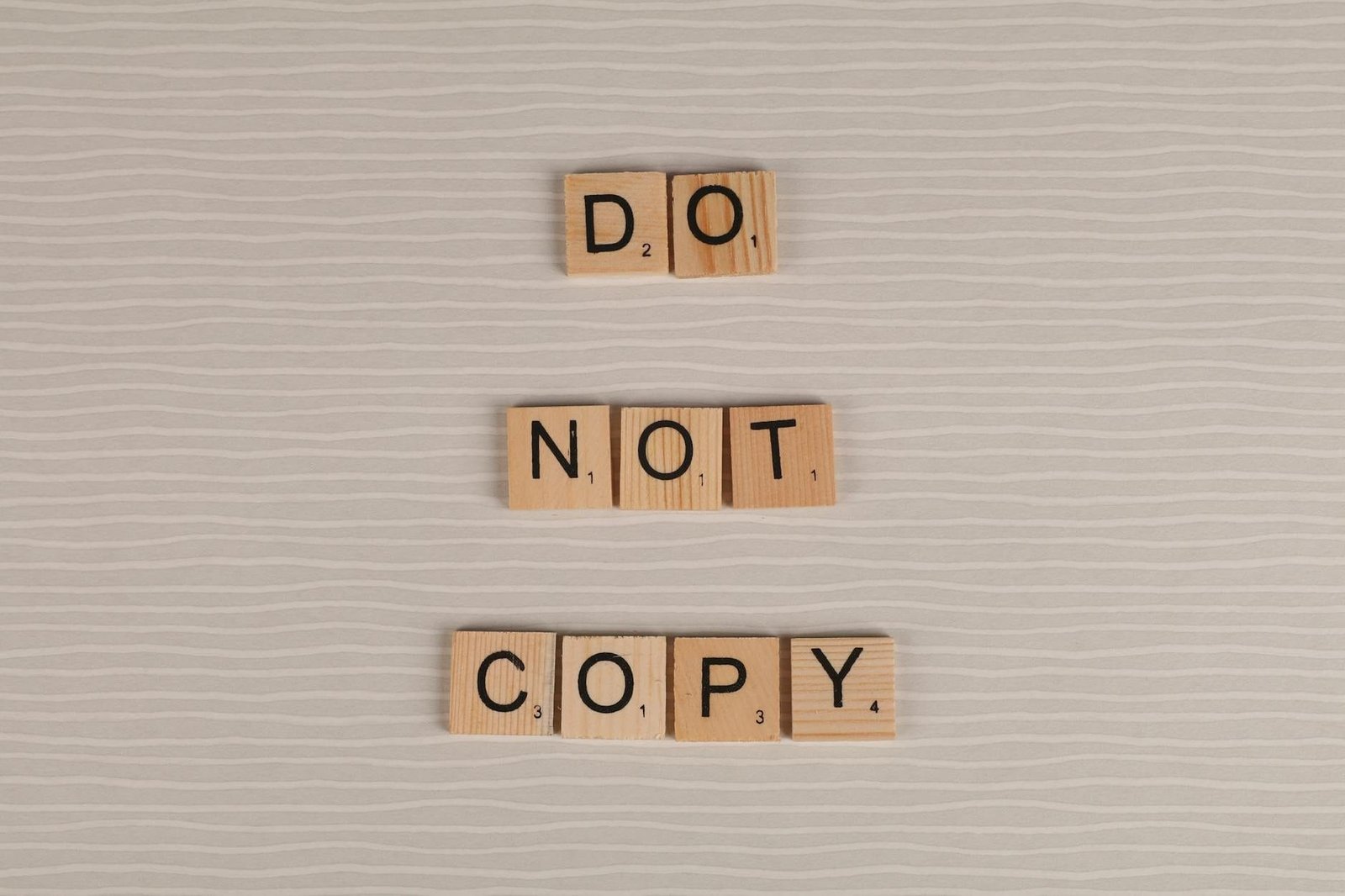 Close-up of wooden tiles spelling Do Not Copy on a textured surface.