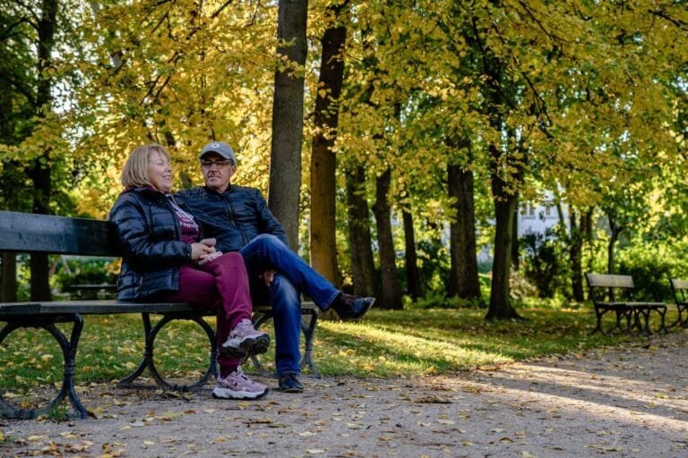 Happy senior couple sitting on a park bench surrounded by autumn foliage.