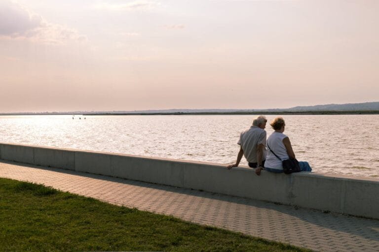 A serene moment of an elderly couple sitting by a lake at sunset, reflecting tranquility.
