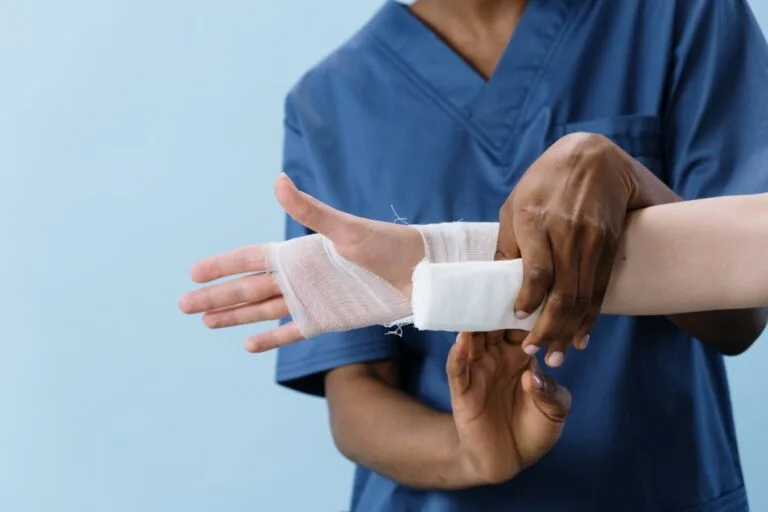 A medical professional carefully wrapping a bandage around an injured persons hand.