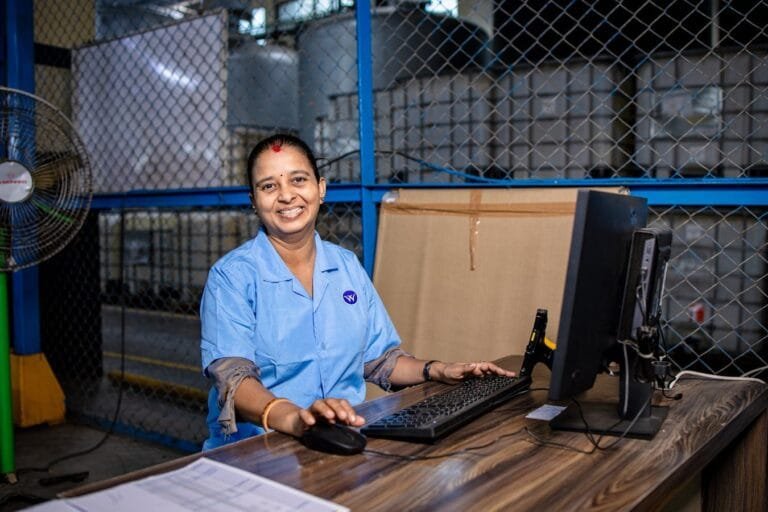 Desvio de Função: Como Provar e Cobrar Diferenças Salariais 2 A cheerful female factory worker in blue uniform working at a computer in an industrial setting.