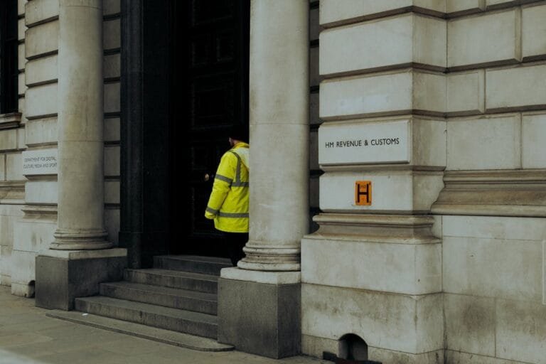 A guard in yellow jacket at the entrance of HM Revenue & Customs building in the UK.