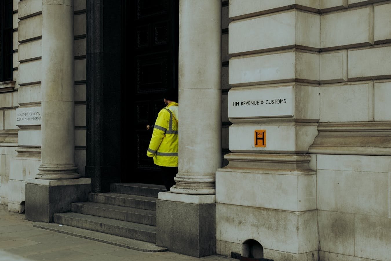 A guard in yellow jacket at the entrance of HM Revenue & Customs building in the UK.
