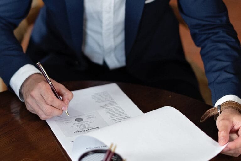 Honorários Advocatícios: Tipos e Como São Cobrados 2 A professional individual signs legal documents at a desk in an office setting.