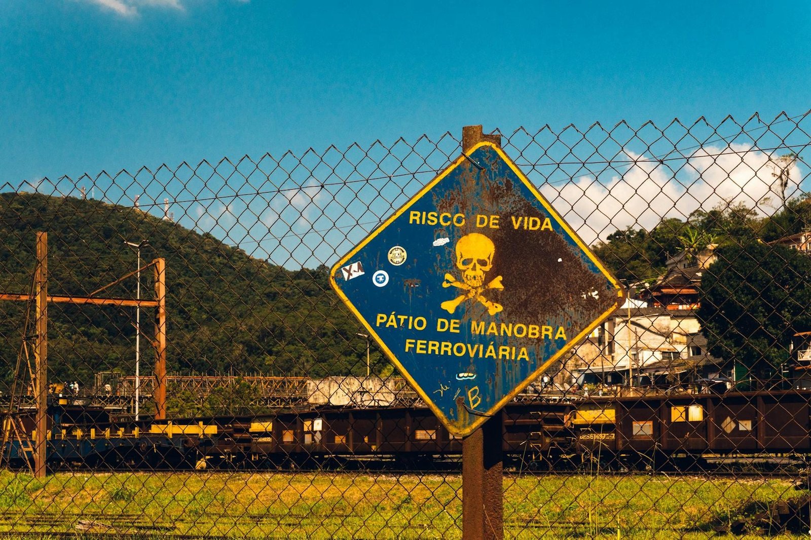 Rusty danger sign at a railway yard in São Paulo, Brazil under a bright blue sky