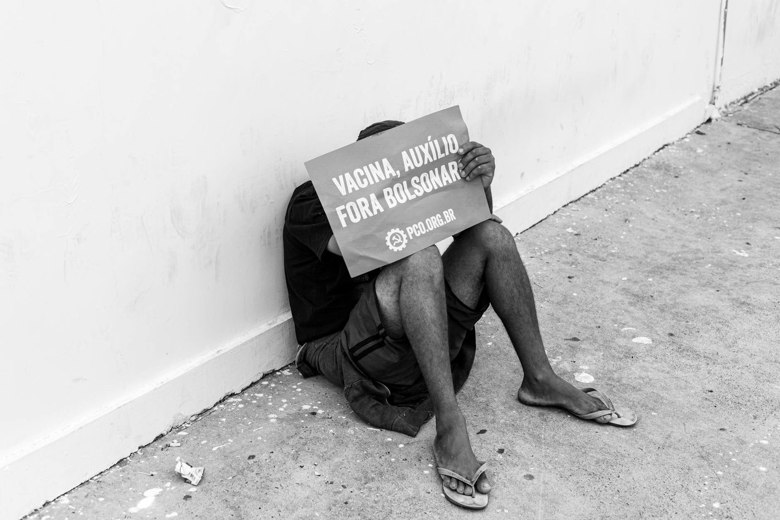 Black and white photo of a protestor holding a sign sitting against a wall.