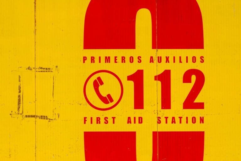 Bright yellow and red emergency sign indicating first aid station. Call 112 for 