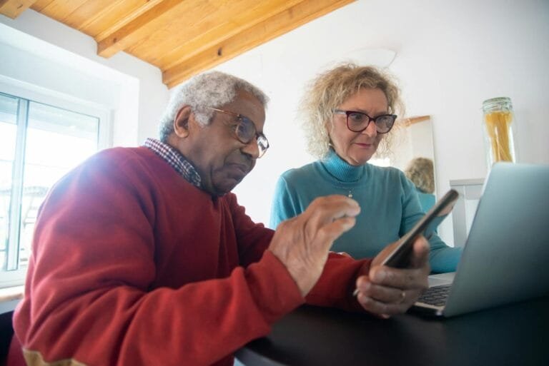 Elderly couple using a smartphone and laptop for online shopping in a cozy home 