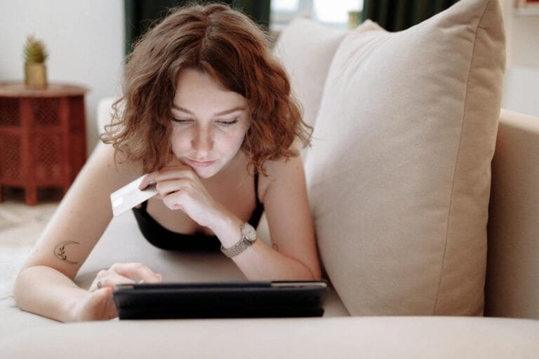 Malha Fina: Como Identificar a Pendência e Regularizar 3 Young woman using a tablet and credit card for online shopping, lying on a couch