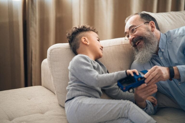A joyful grandfather and grandson sharing a playful moment on the couch, indoors