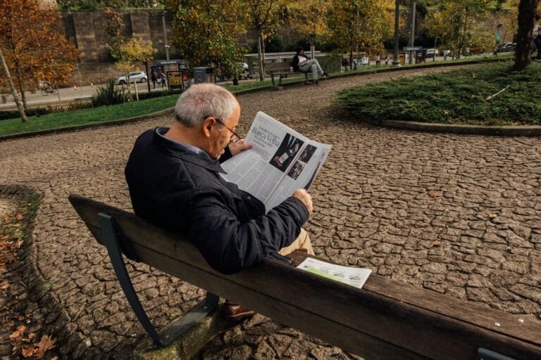 Senior man enjoys reading the newspaper while relaxing on a park bench in Porto,