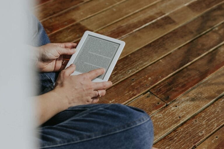 Close-up of hands holding an e-reader on a wooden floor, depicting a casual read