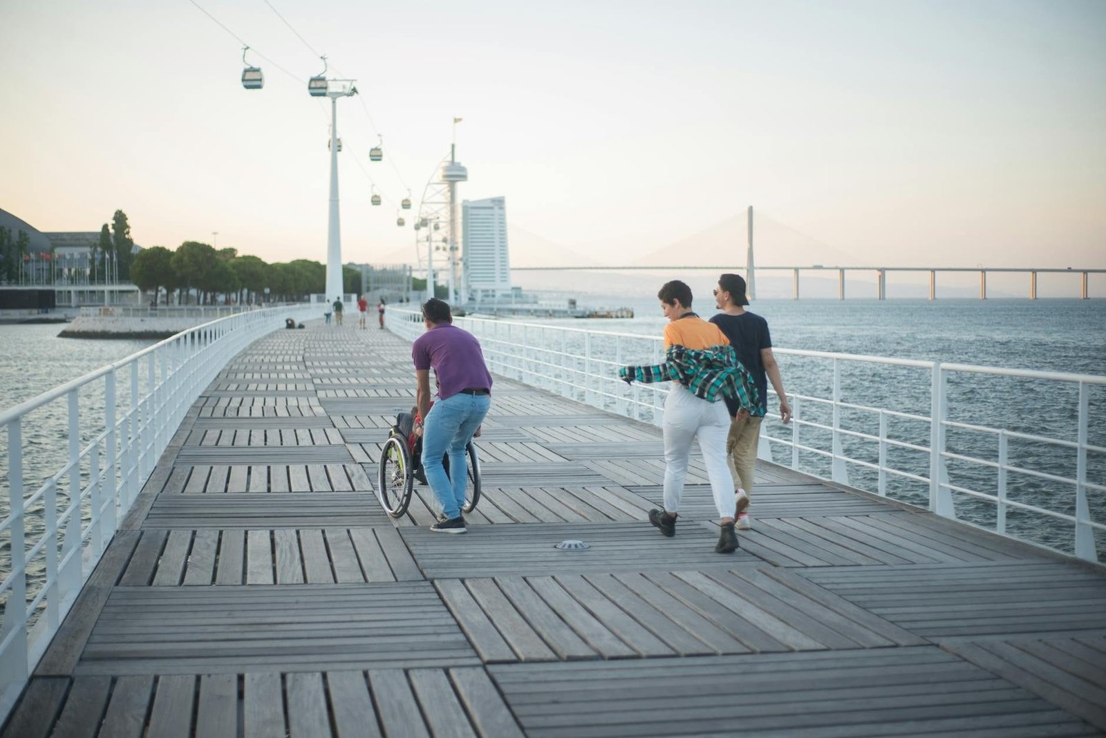 Aposentadoria por Invalidez: Critérios da Perícia Médica 1 Three friends enjoy a sunset walk along a scenic Lisbon boardwalk with a wheelch