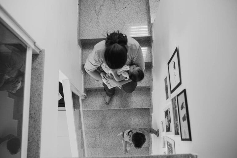 BPC/LOAS: Cálculo da Renda Familiar per Capita 6 A mother carrying a baby descends a staircase with a young child in a modern hom