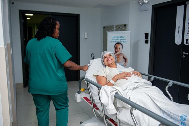 BPC/LOAS: Quem Tem Direito ao Benefício Assistencial 12 A caring nurse assists a patient in a hospital corridor with a joyful demeanor.