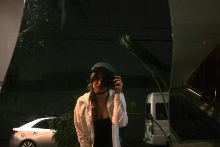 Woman taking a selfie at night, reflecting in a window, outdoors.