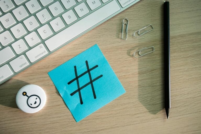 Top view of hashtag symbol on sticky note with keyboard and stationery on desk.