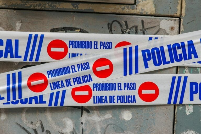 Police tape with Prohibido El Paso against graffiti-covered wall. Crime scene 