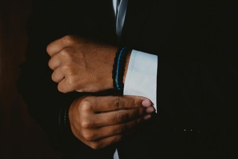 Crop unrecognizable stylish man in formal suit and wristband buttoning up white 