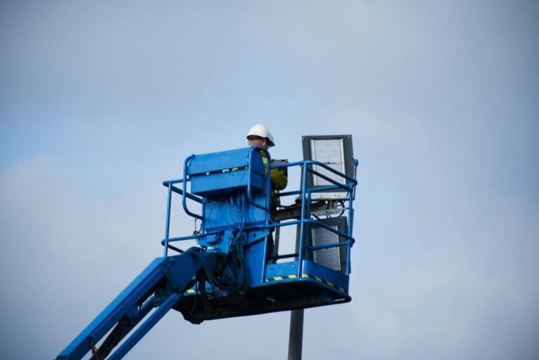 An industrial worker wearing a hard hat operating a lift platform for maintenanc
