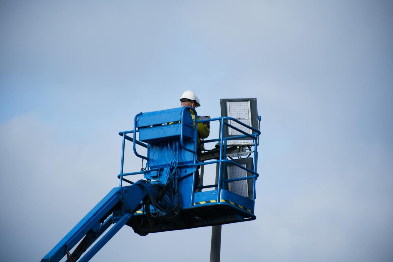 An industrial worker wearing a hard hat operating a lift platform for maintenanc