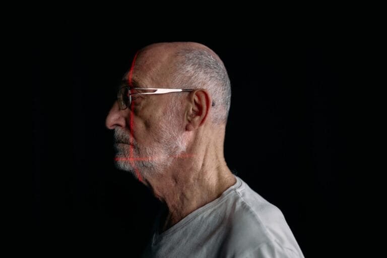Prova de vida do INSS pode ser feita por reconhecimento facial 6 Side profile of a senior man with facial recognition scan lines on a plain black