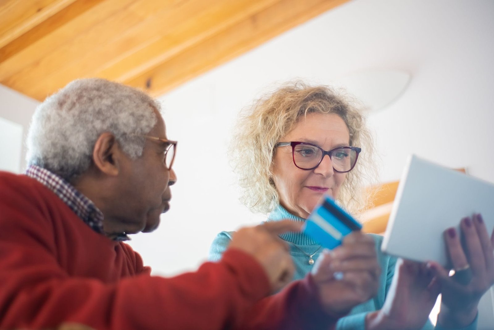 INSS antecipa o 13º de aposentados e pensionistas em 2026 1 Senior adults using a tablet and credit card for online shopping indoors.