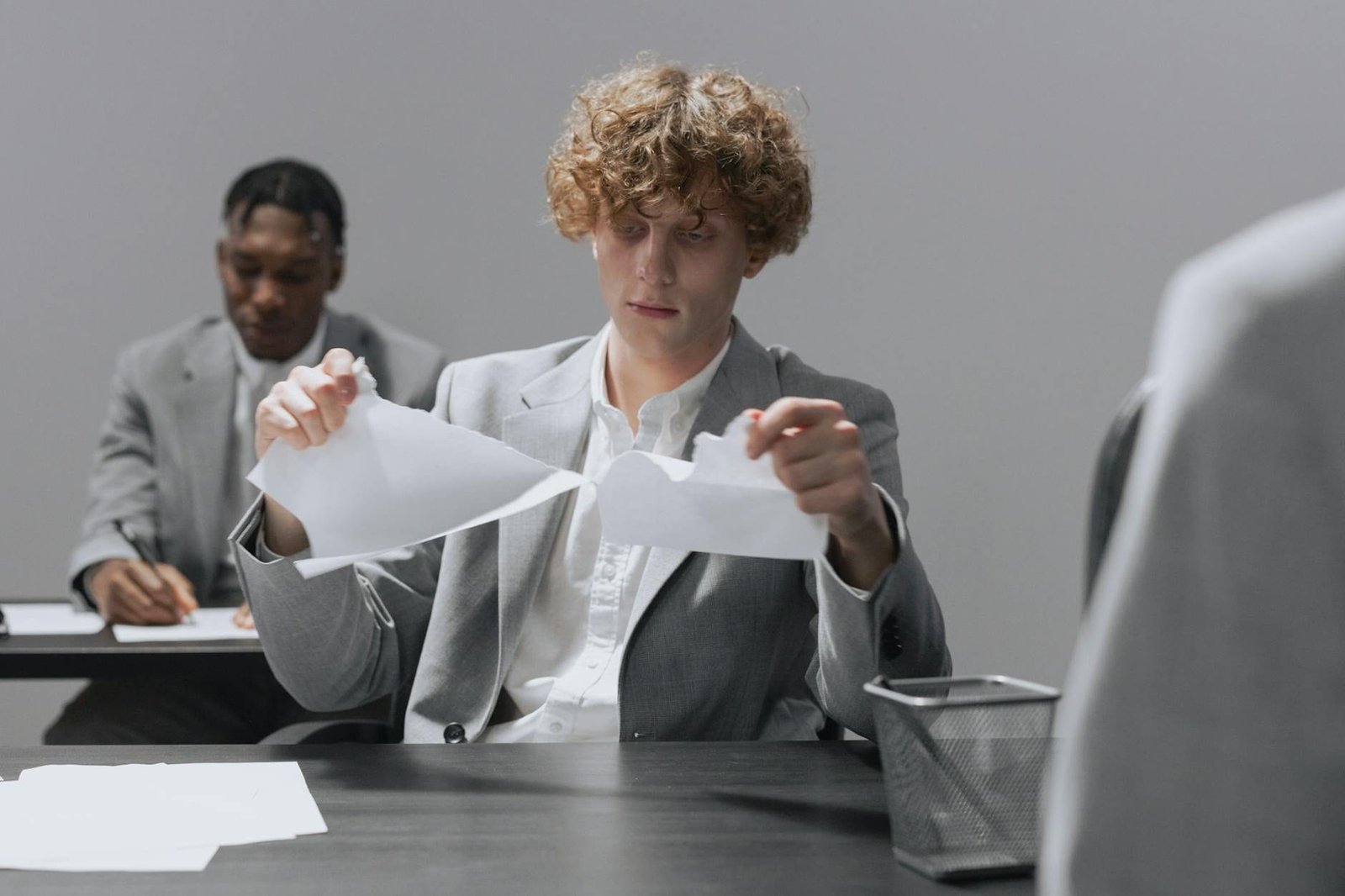 Two employees in suits sitting at desks, one tearing paper.