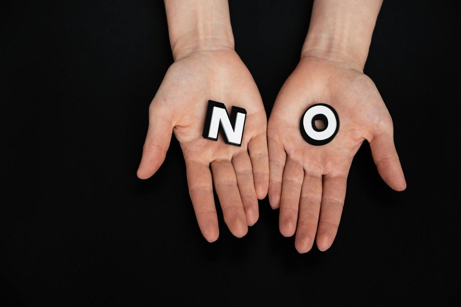 Close-up of open palms holding letters spelling NO on a black background.