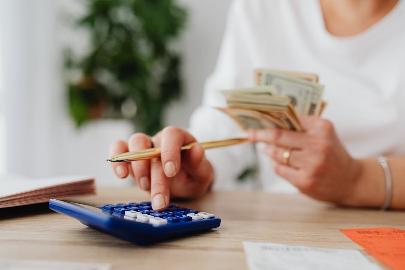 INSS já ressarciu mais de 4 milhões por descontos indevidos 1 A person sits at a desk calculating finances using a calculator and holding cash.