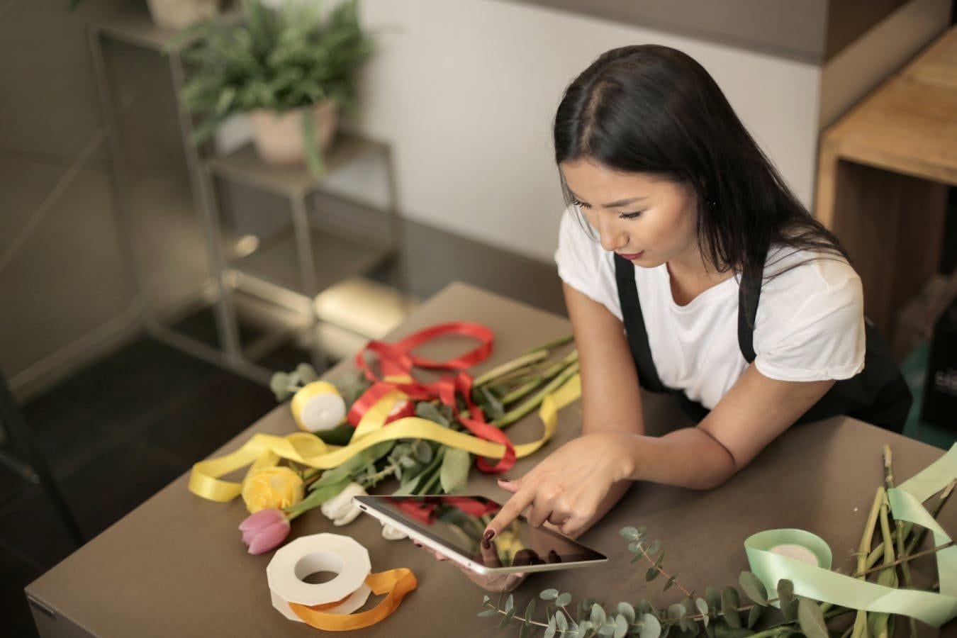 Florist using a tablet while arranging a colorful bouquet in a shop indoors.