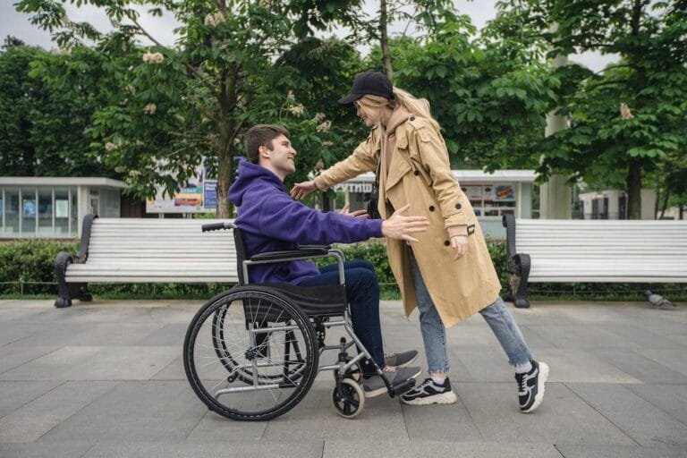 A man in a wheelchair and a woman greet each other warmly in a park setting.