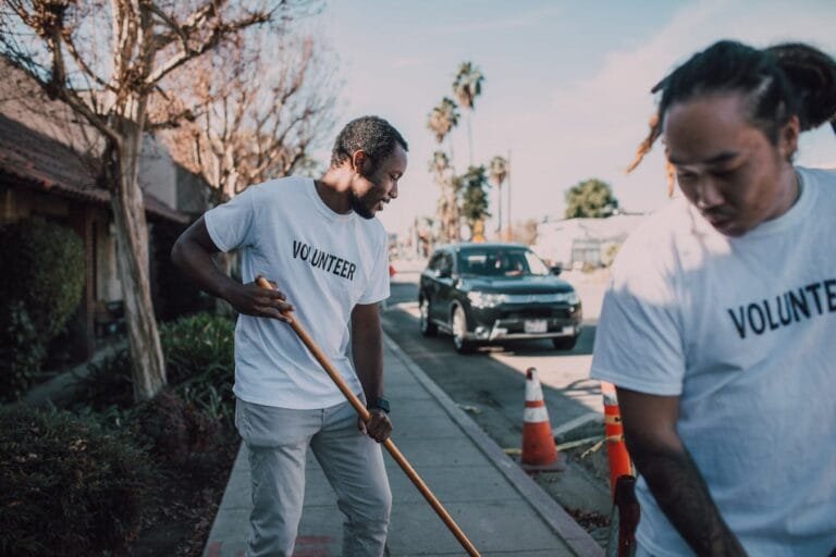 Two volunteers working together to clean a sidewalk on a sunny day.